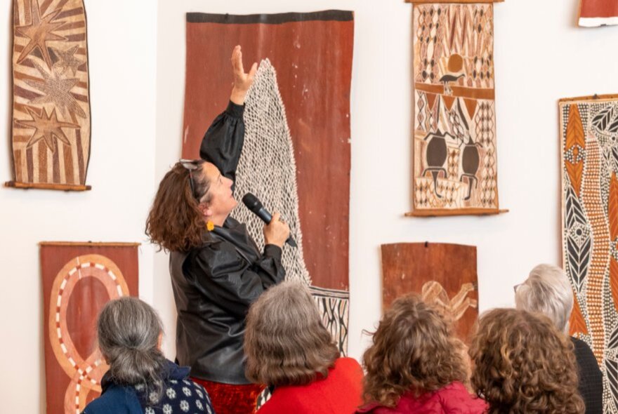 Tour eader pointing to Indigenous artworks on a gallery wall with tour participants looking on.