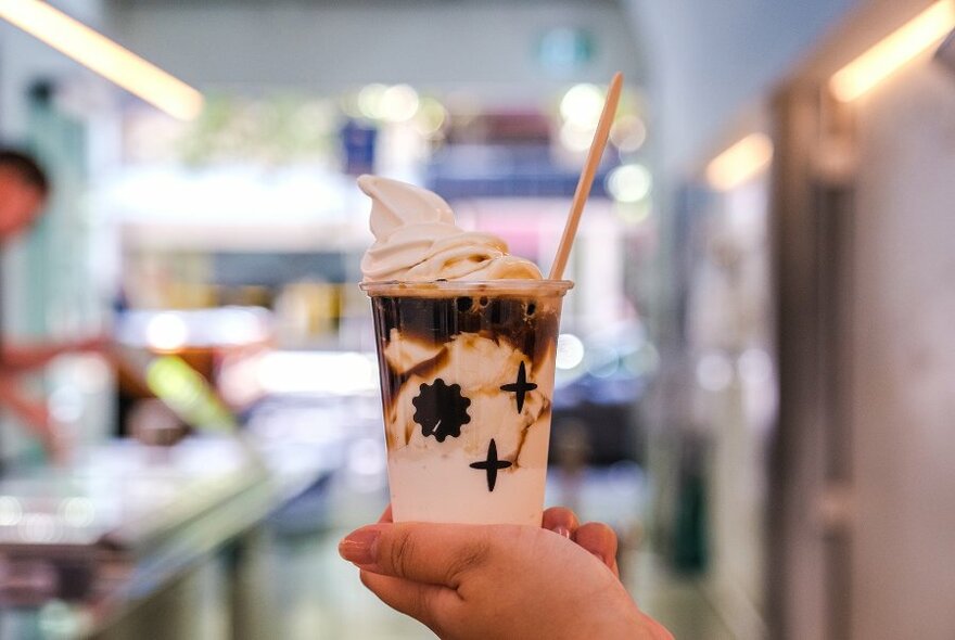 Someone holding out a takeaway milk drink with a swirl of ice cream on top.