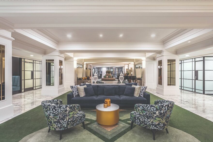 Hotel public area with marble and white details, art deco design, and blue furnishings.