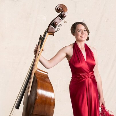 Classical musician holding a cello, wearing a long red satin gown.