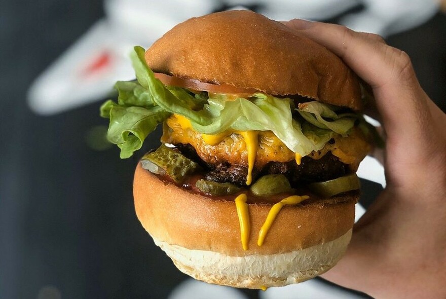 Hand holding a hamburger spilling mustard.