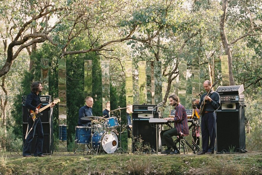 The four piece band Mildlife playing on their instruments with amplifiers and speakers, in a forest.