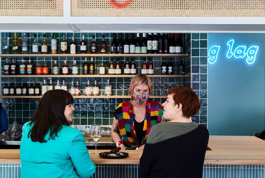 Two diners sitting at the bar and being served food and wine. 