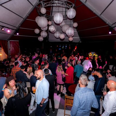 People gathered under a tented outdoor event roof with hanging lights.