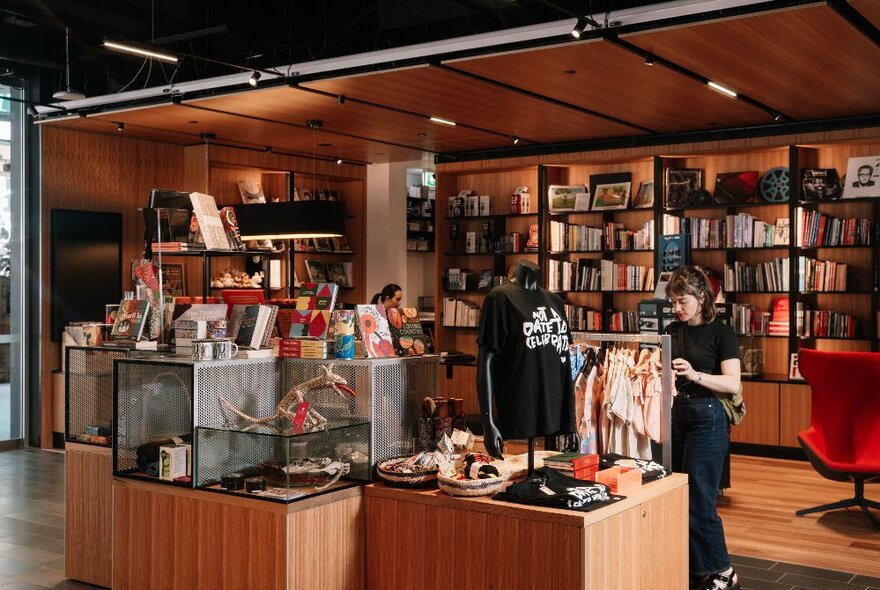 A museum gift shop with timber shelves and displays and staff attending. 