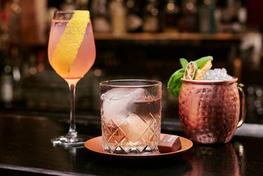 Three cocktails in different shaped glasses lined up on a bar.