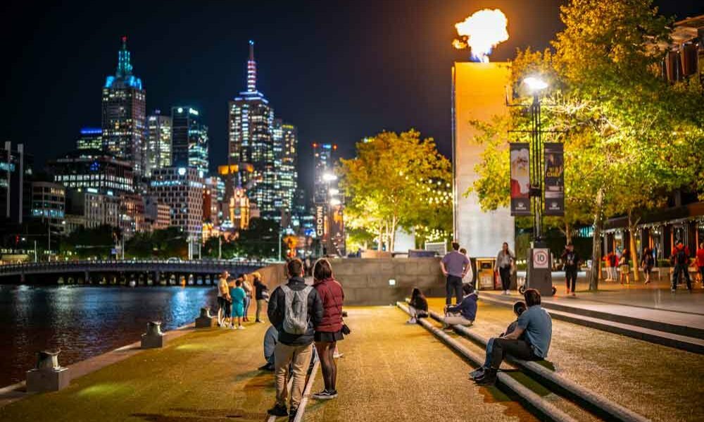 People beside the river watching a flame tower installation