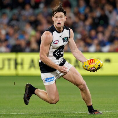 A Carlton AFL football player running with the ball in a stadium during a footy match.