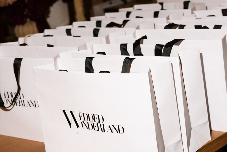A row of white showbags at a wedding expo with the words Wedded Wonderland in black print on the front of them.