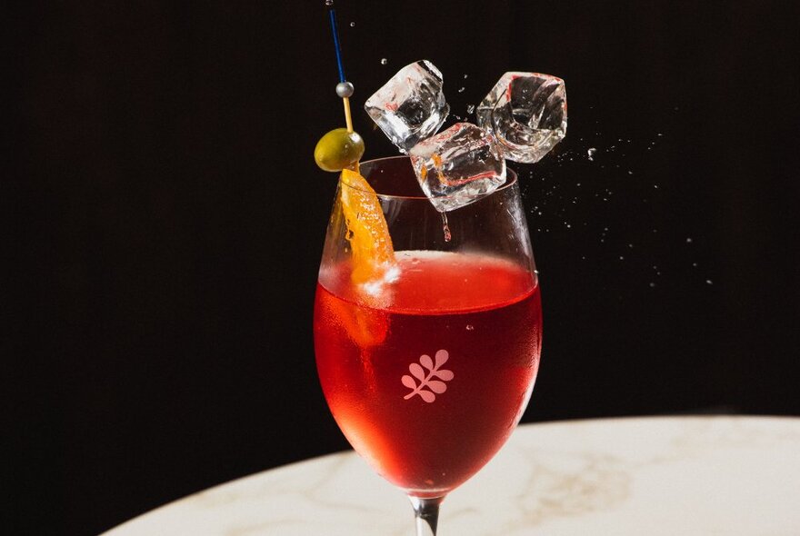 Red liquor in a cocktail glass with ice cubes and garnish.