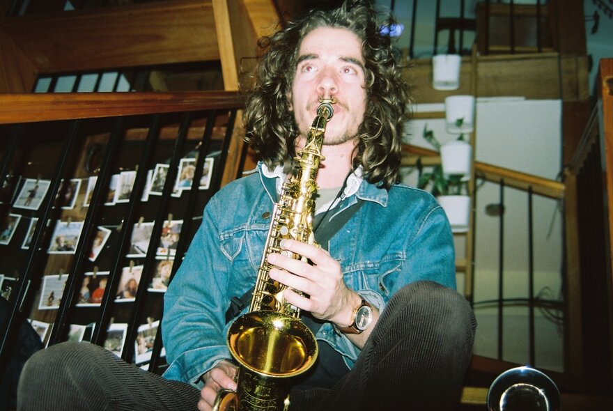 Musician, Anthony Probyn, playing the saxophone wearing a denim jacket and dark jeans.