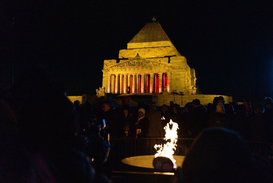 The Shrine of Remembrance illuminated in the darkness while people gather around the Eternal Flame. 