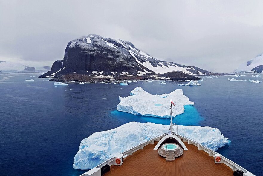 Image of a rocky glacier in the Antarctic sea with the bow of a ship just visible in the foreground