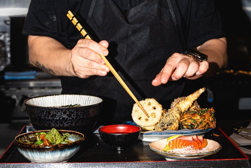 A chef placing an item of food on a plate using chopsticks.