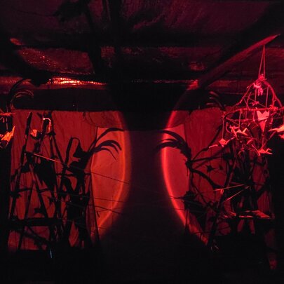 A dark stage with two dark red lights showing puppets and shapes. 