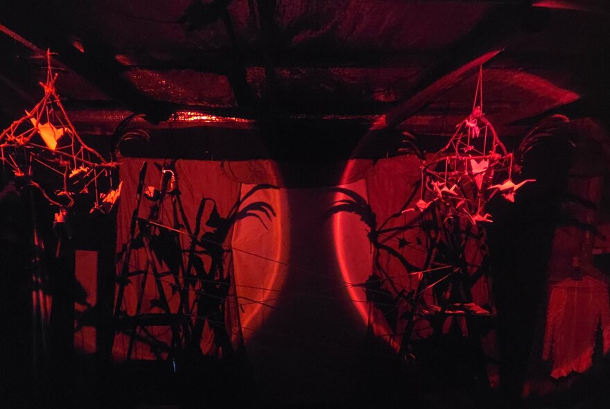 A dark stage with two dark red lights showing puppets and shapes. 
