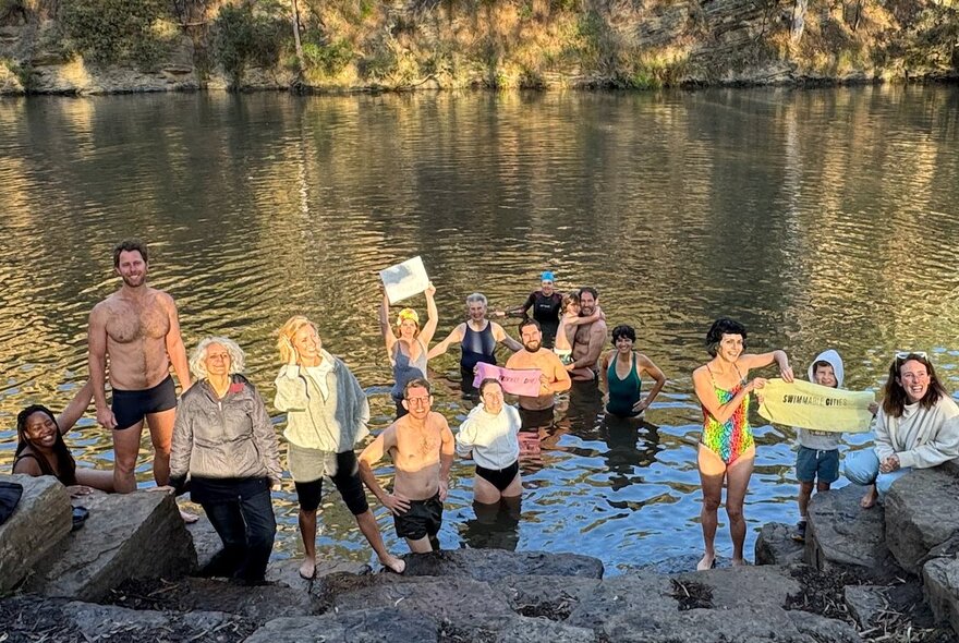 A still from the documentary Big Swim, depicting a group of people in bathing costumes, at the banks of a river, some of them half in the water.