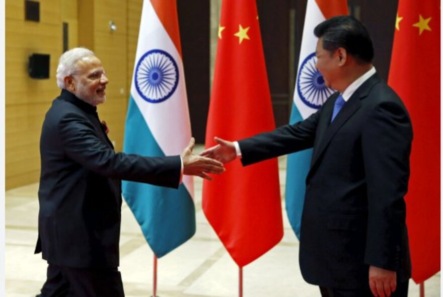 Two world leaders shaking hands in front of nation flags.