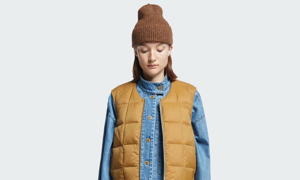 A model wearing a brown beanie, denim shirt and brown puffer vest.