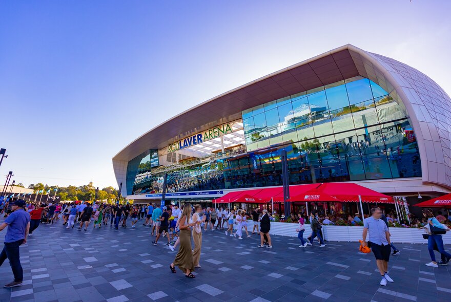 A crowd of people are walking past Rod Laver Arena at the Australian Open tennis tournament