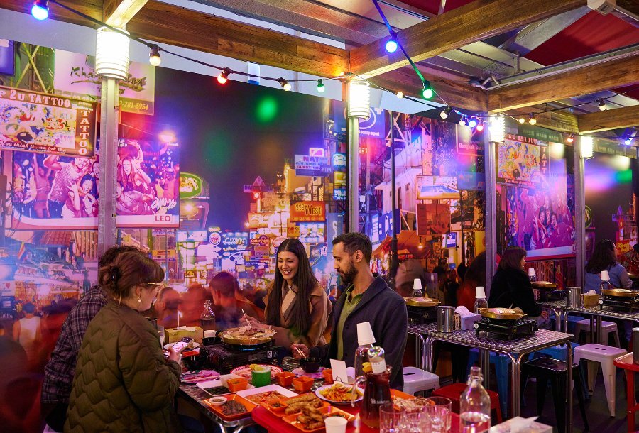 A group dining on hotpot in a colourful restaurant with a Bangkok mural on the wall.