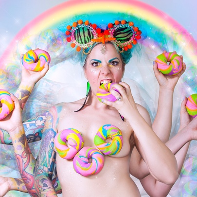 An image of a naked woman with multiple arms and hands all holding pastel-coloured doughnuts with a rainbow over her head. 