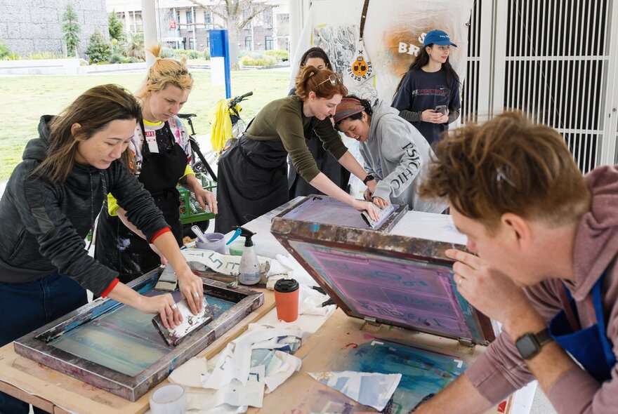A group of people screenprinting at a craft workshop in an outdoor space.