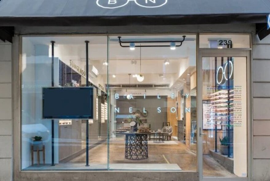 The shopfront of an eyeglass store, with large windows and shelves of eyeglasses seen from the outside.