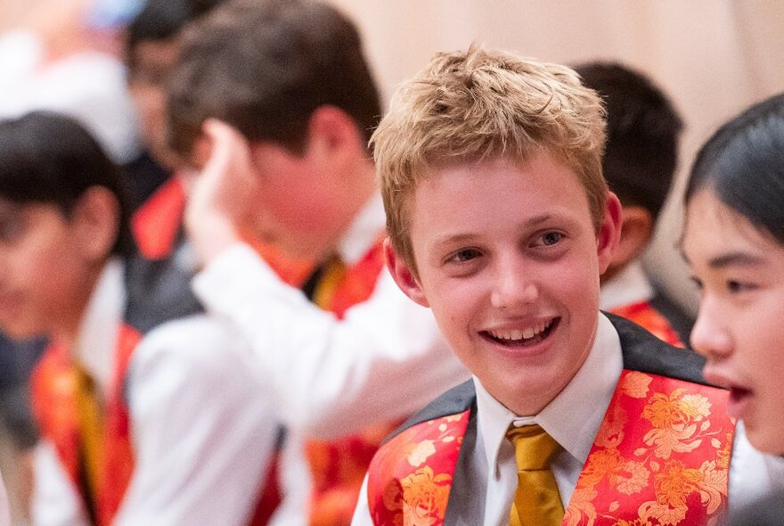 Smiling boys wearing white shirts, gold ties and Christmas-themed silk vests as they sing carols.