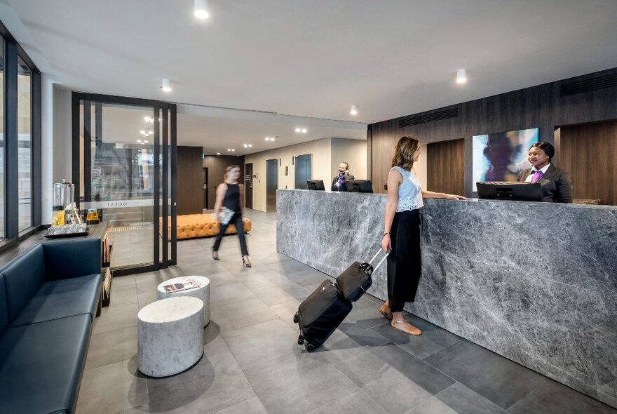 The lobby and concierge area at Quest NewQuay, with a person carrying baggage checking in at reception.