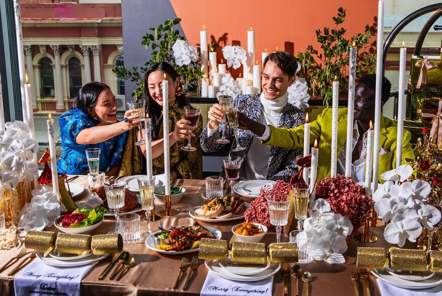 A restaurant table filled with platters of food, glasses of wine, candles and festive decorations, with a group of four people raising their glasses in a toast.