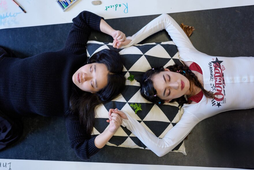 Looking down on two women sharing a cushion head-to-head and linking hands. 