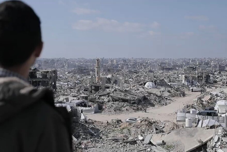 The outline of a figure looking at an endless vista of devastated bombed buildings and roads.
