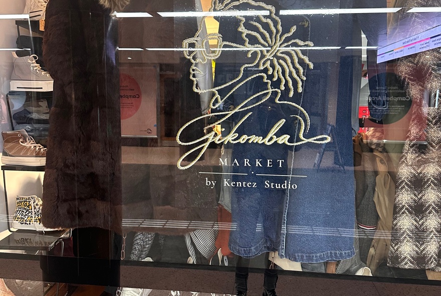 The glass storefront window of Gikomba Market located in Campbell Arcade, with fashion items displayed in the window.