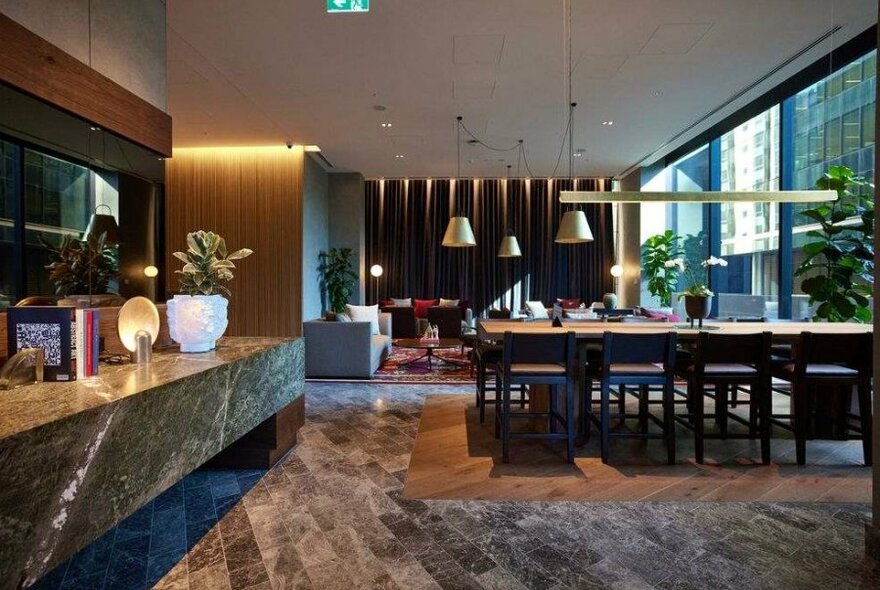 A stylish hotel lounge with communal tables and a marble desk.