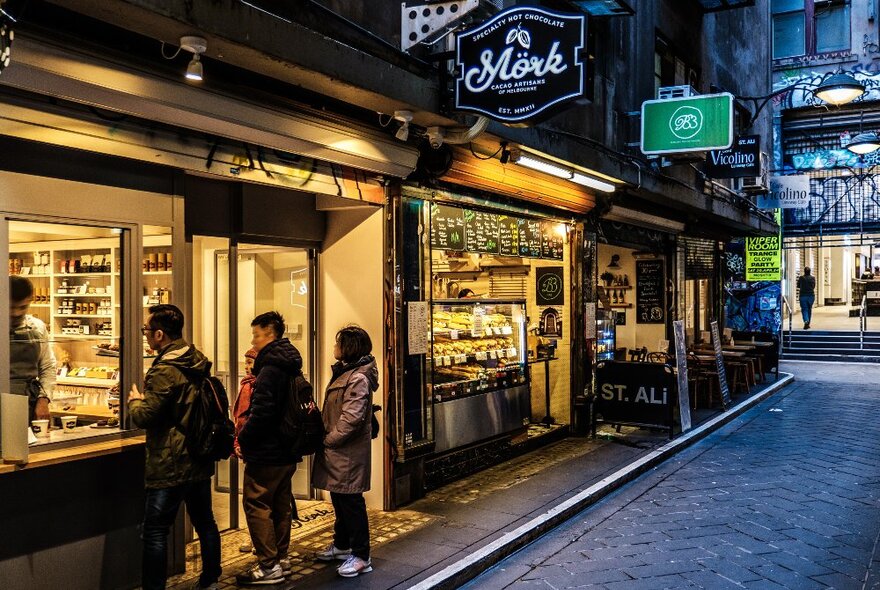 A group of people are ordering a hot chocolate from a laneway cafe.