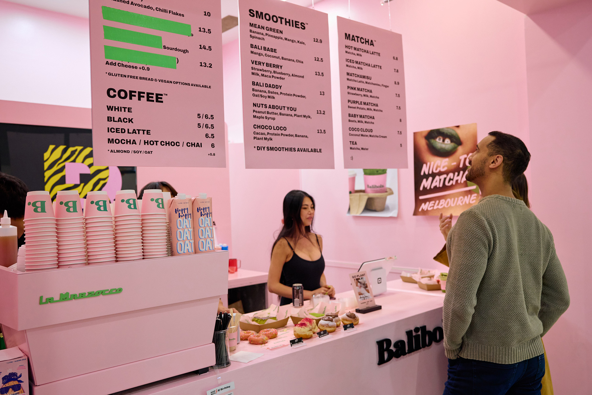 A person is standing behind a counter at a pink matcha shop a customer is looking at the menu