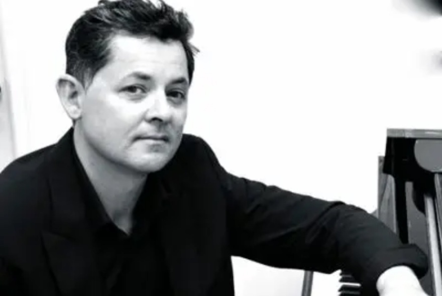 A black and white portrait of a man resting his arm on the top of a black piano.