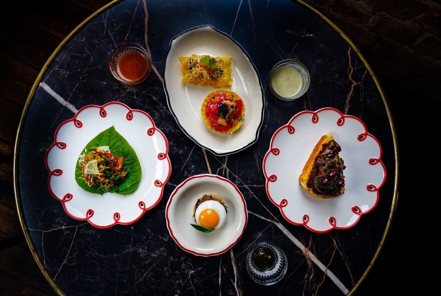 Looking down at four plates of carefully arranged Thai food on white plates.