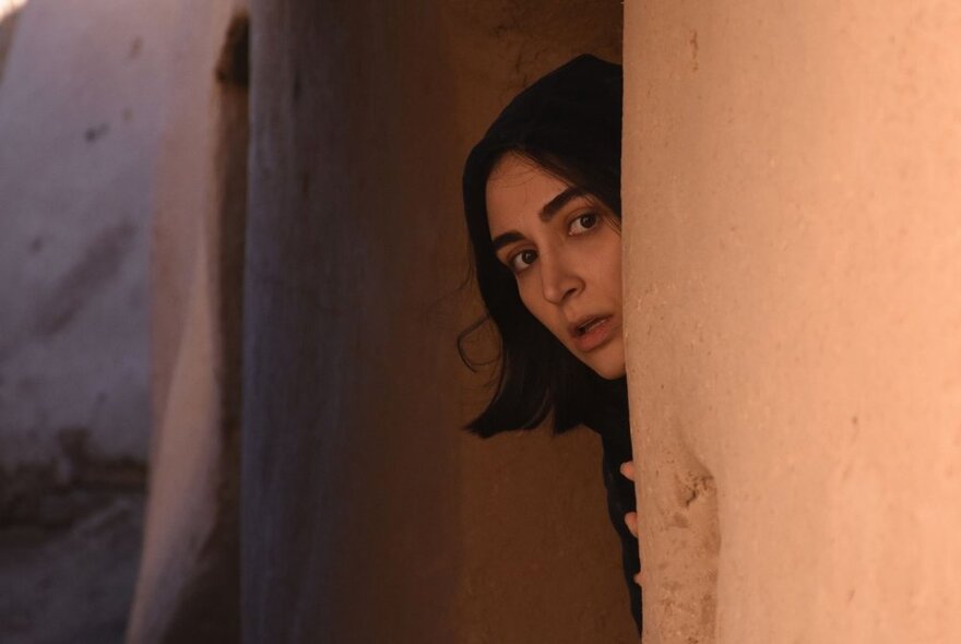 A young woman peeking around a corner in a dark area. 