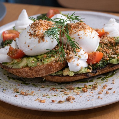 Poached eggs, mashed avocado and cherry tomatoes served on toast on a plate.