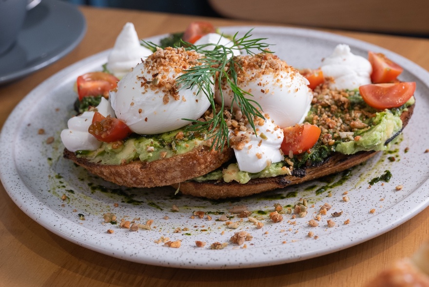Poached eggs, mashed avocado and cherry tomatoes served on toast on a plate.