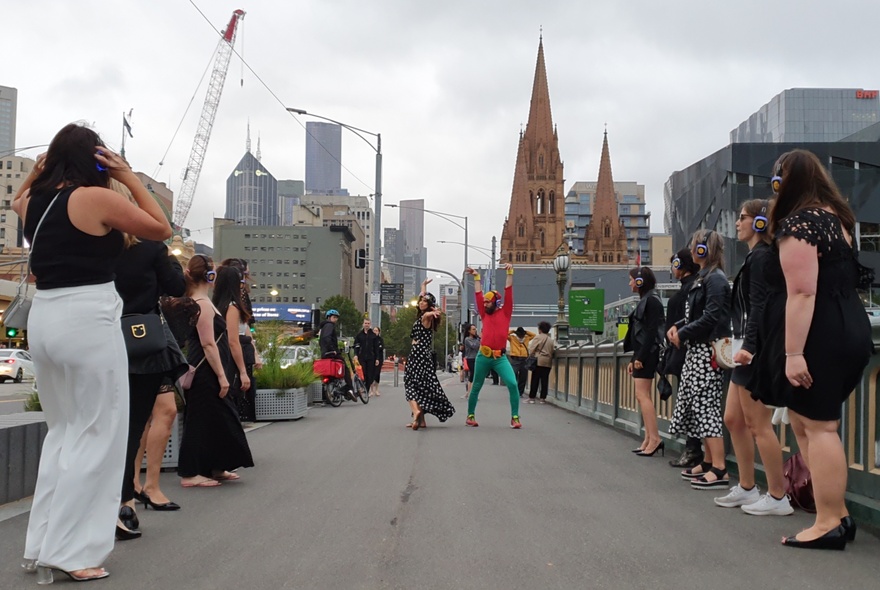 People taking part in a silent disco dance-walk  with a host tour guide, walking across Melbourne's Princes bridge. 