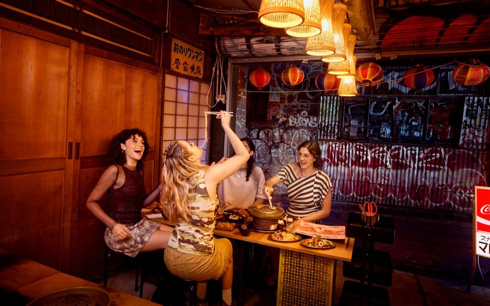 Four women sitting at a wooden table, talking while eating hotpot.