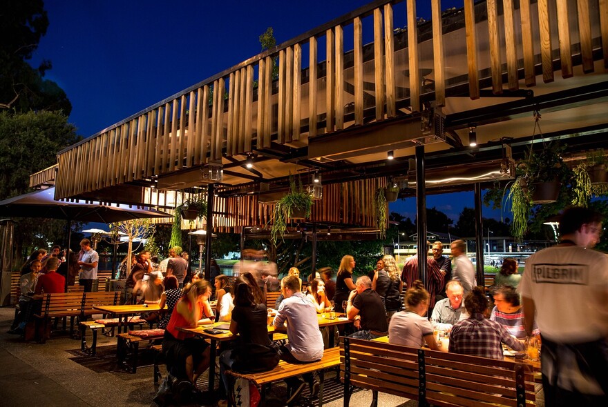 People drinking and dining at tables outside Pilgrim Bar in the evening.