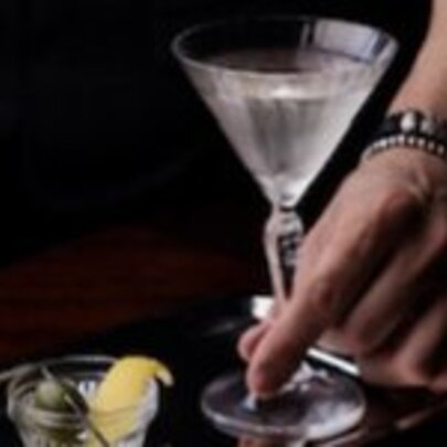 Hand holding a martini with garnish of lemon and olive in separate dish.