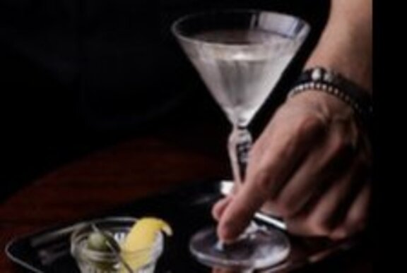 Hand holding a martini with garnish of lemon and olive in separate dish.