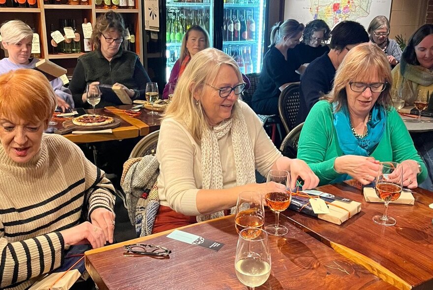Three women sitting at a table with glasses of wine in a bar settiing.