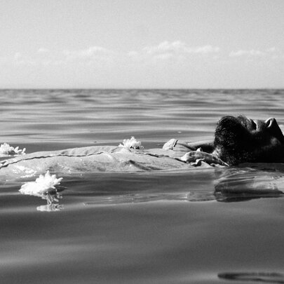 Bearded man floating in a still sea, his chest rising above the water.
