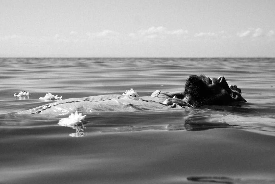Bearded man floating in a still sea, his chest rising above the water.